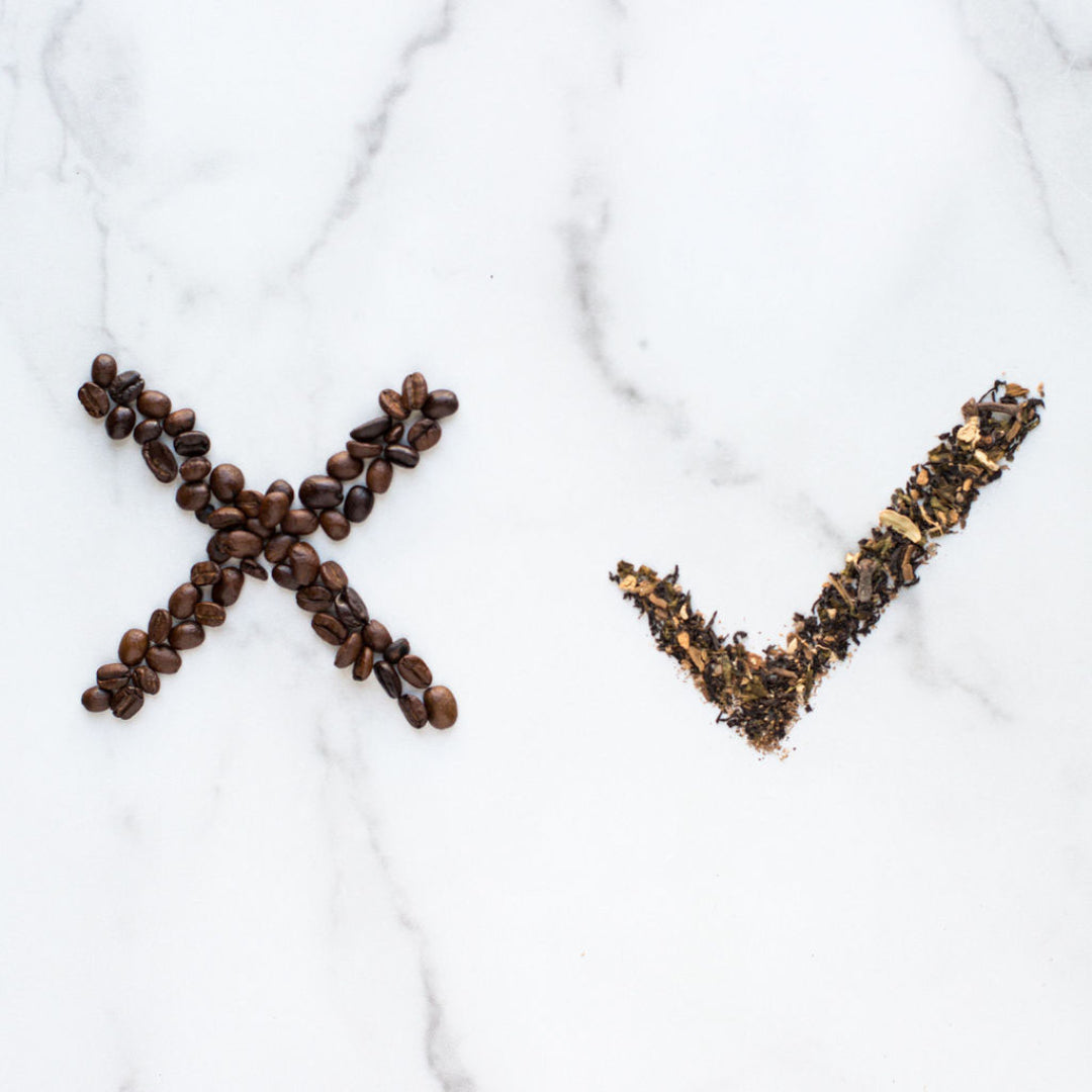 Coffee beans arranged in an X shape and tea leaves forming a checkmark on a white marble surface.